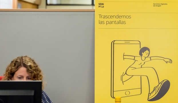 Una mujer trabajando en la oficina de SDA, al fondo se ve un cartel amarillo con el lema 